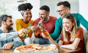 A group of young people enjoying pizza and beer while laughing together.