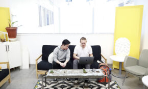 Two students sit on a couch in a small lounge area at ECU, facing the camera but looking at a laptop together.