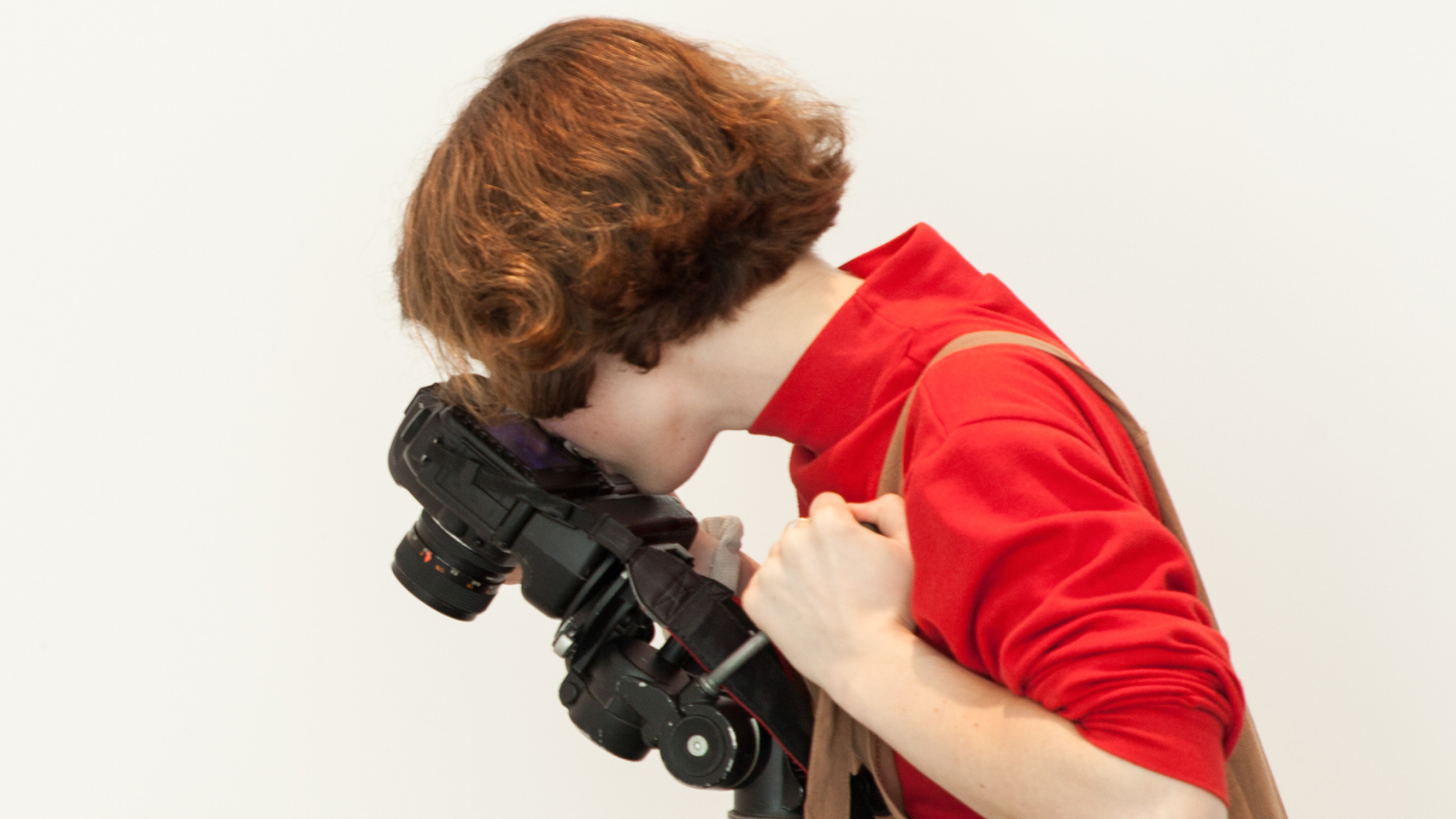 A student looks through a camera, angled down at something out of frame.