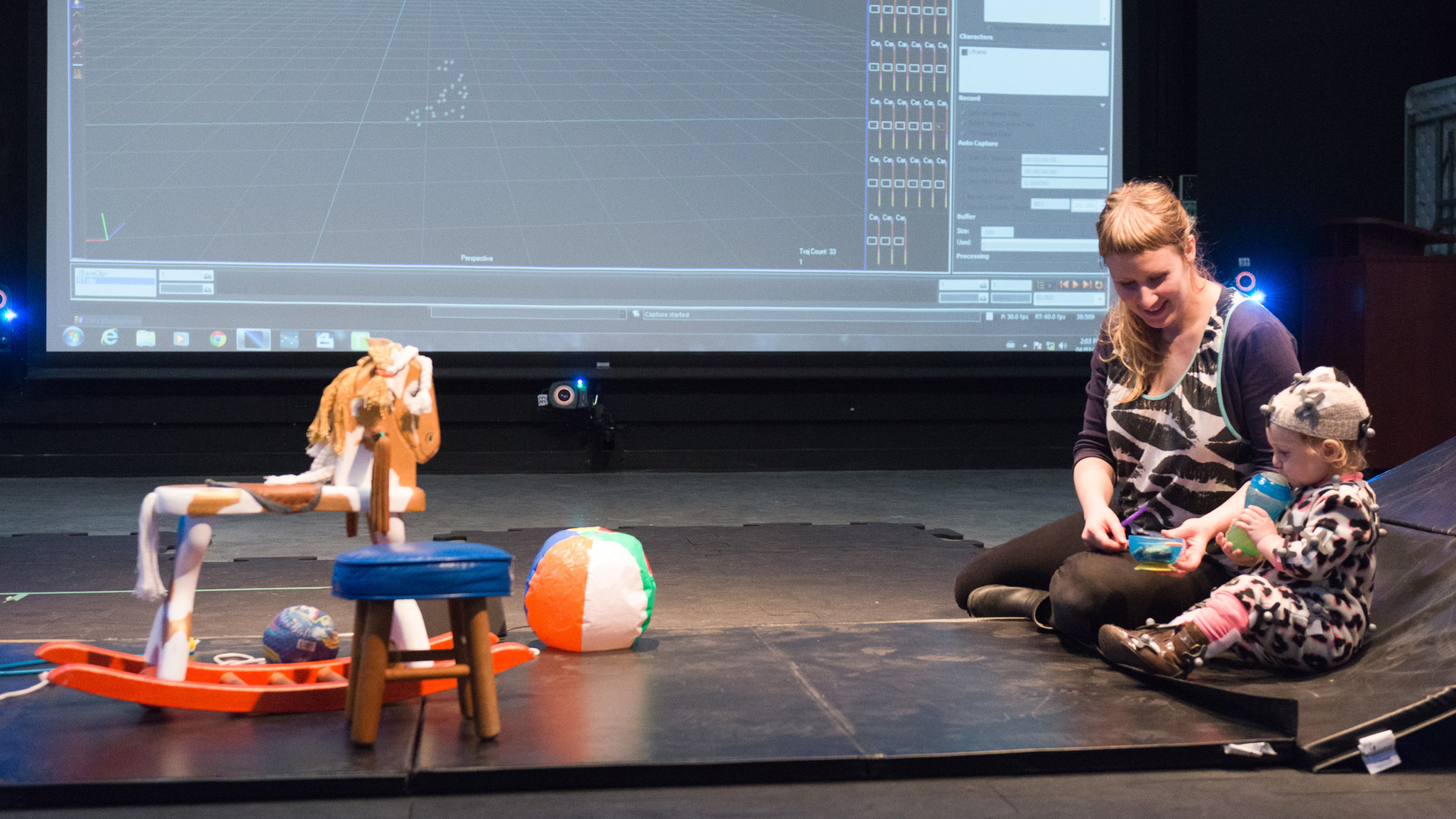 A woman and a small child sit in ECU's Integrated Motion Studio, looking at a collection of toys in front of a large screen.