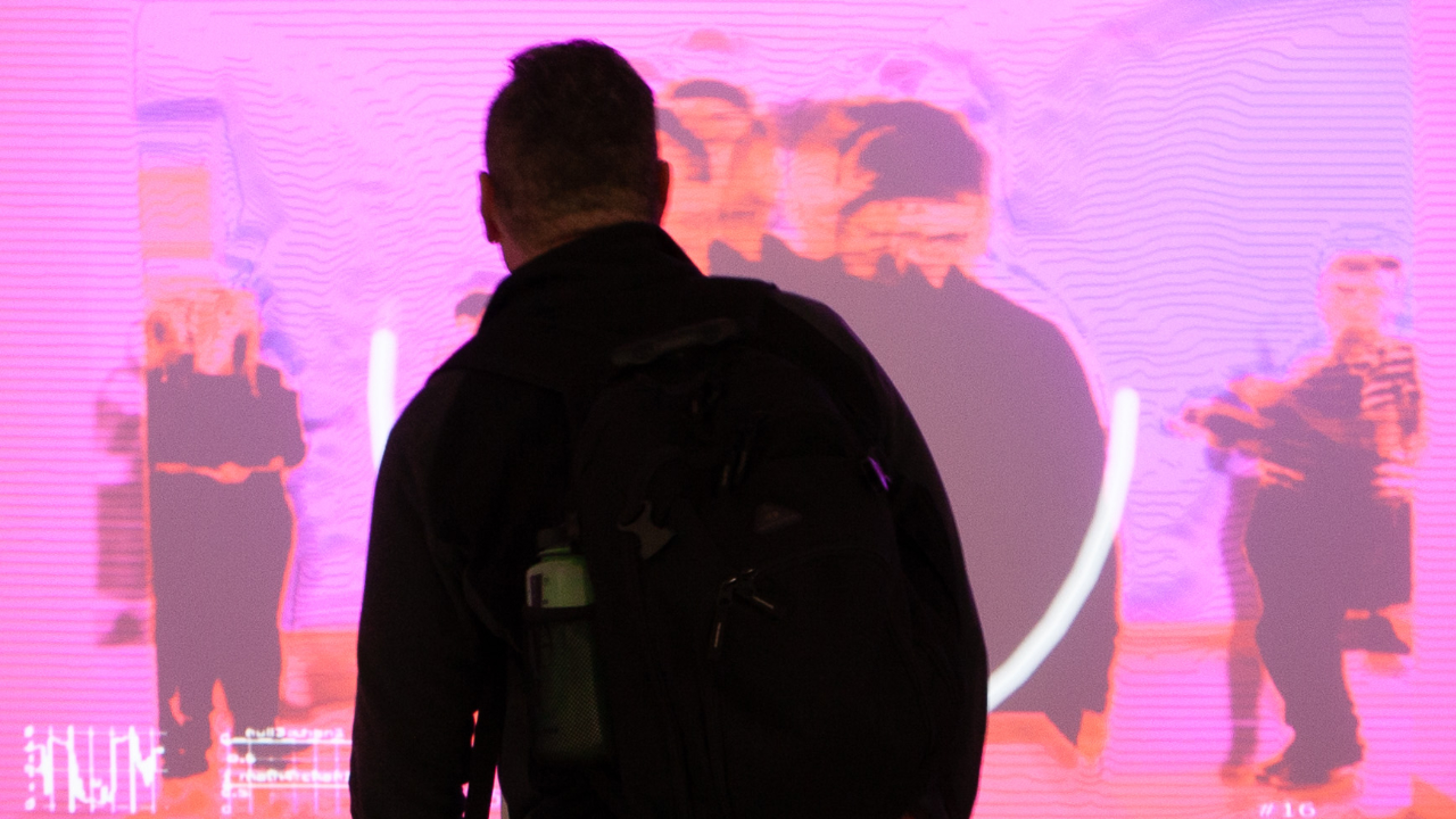 A person stands in front of a screen with their back to the viewer, silhouetted by the light of the screen.