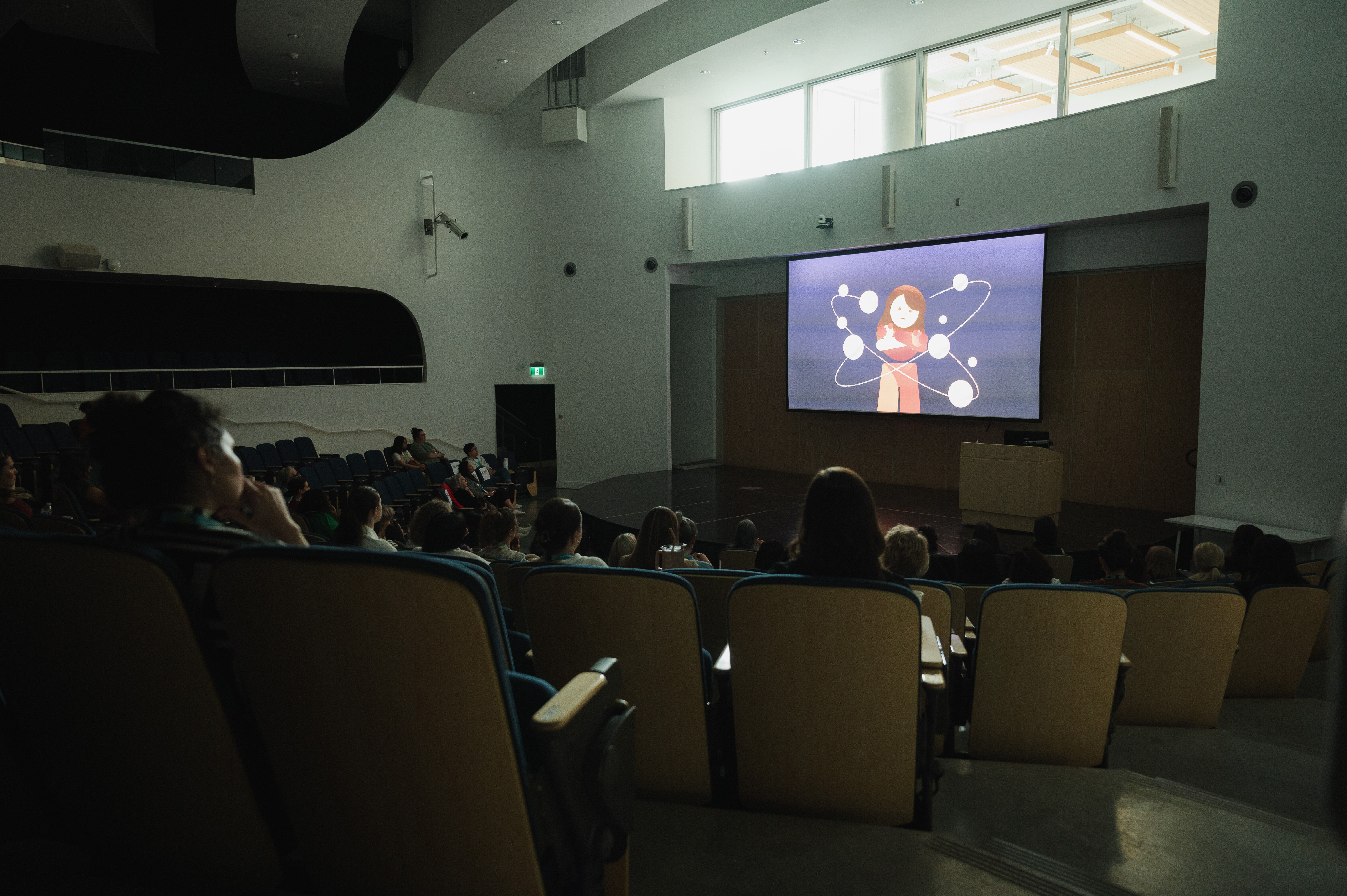 An animated video on a screen being shown to an auditorium of people at the Reliance Theatre