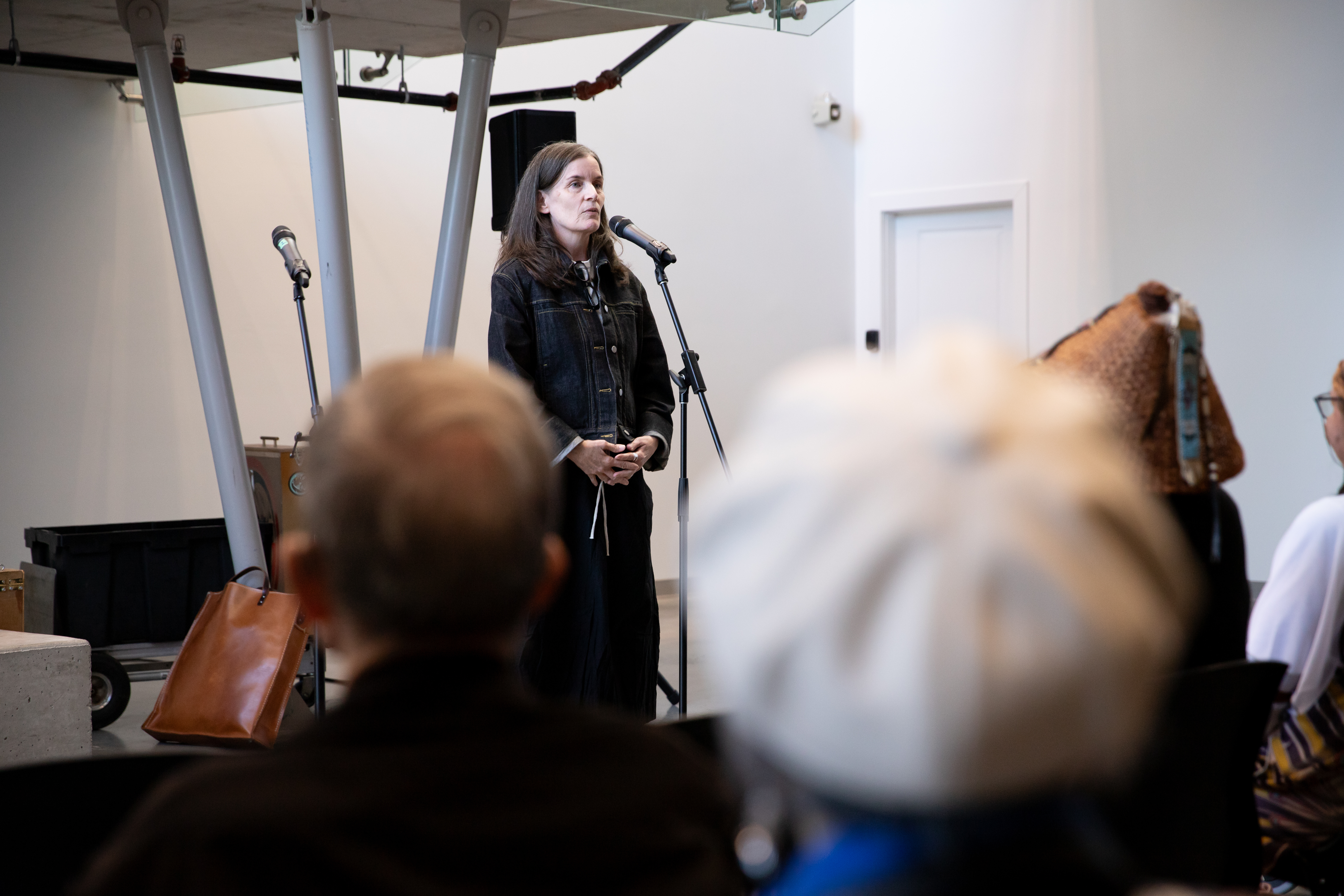 A woman in grey jumper speaks to a crowd in the background