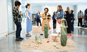 A group of four people look down at an artwork on the lower ground with sand