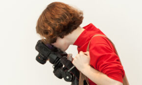 A student looks through a camera, angled down at something out of frame.