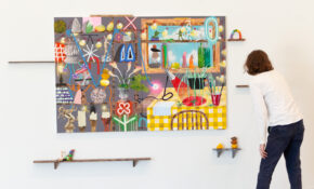 A person looks closely at a colourful canvas hanging on a wall.