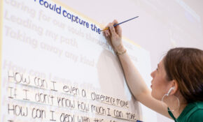 A student paints words on a wall as part of a project.