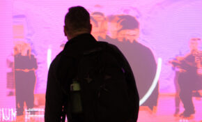 A person stands in front of a screen with their back to the viewer, silhouetted by the light of the screen.