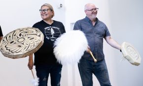 A woman and man with drums stand together in front of a crowd