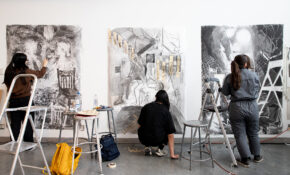 Three people work on large black-and-white drawings side-by-side in a studio.